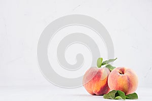 Elegance ripe peaches with green young leaves on white soft wood background, copy space.