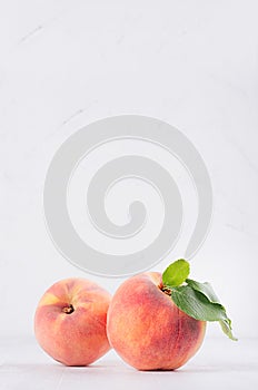 Elegance ripe peaches with green young leaves on white soft wood background, copy space, vertical.