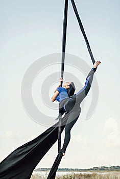 Elegance young beautiful woman dance with aerial silk on a sky background. Fly yoga sport