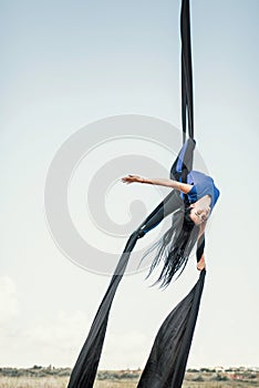 Elegance young beautiful woman dance with aerial silk on a sky background. Fly yoga sport