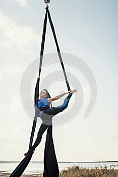 Elegance young beautiful woman dance with aerial silk on a sky background. Fly yoga sport