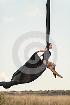 Elegance young beautiful woman dance with aerial silk on a sky background. Fly yoga sport