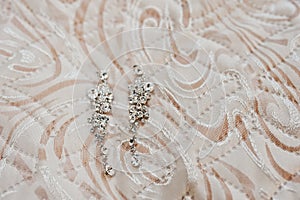 Elegancy wedding brilliant earrings of bride on texture.