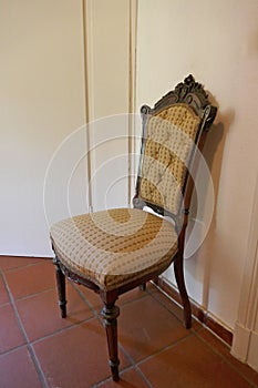 Elegant antique upholstered chair with carvings, in front of white wall.
