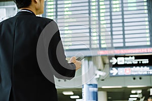 Elegant asian businessman checking email on mobile phone while walking with suitcase inside airport