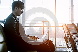 Elegant asian businessman checking email on mobile phone while walking with suitcase inside airport