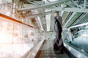 Elegant asian businessman checking email on mobile phone while walking with suitcase inside airport