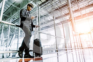 Elegant asian businessman checking email on mobile phone while walking with suitcase inside airport