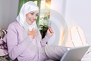 Elegant attractive Muslim woman using mobile laptop searching online shopping information in living room at home. Portrait of