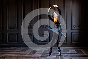 Elegant ballerina in black tutu and pointe shoes dancing on dark gray background