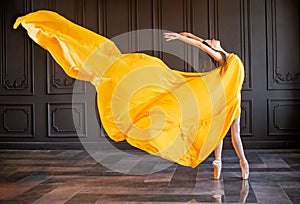 Elegant ballerina in pointe shoes dances with flowing yellow fabric on a dark gray background