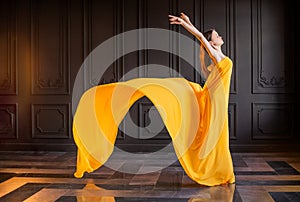 Elegant ballerina in pointe shoes dances with flowing yellow fabric on a dark gray background