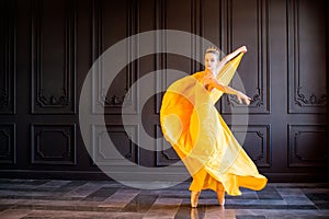 Elegant ballerina in pointe shoes dances with flowing yellow fabric on a dark gray background