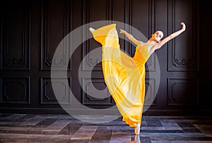 Elegant ballerina in pointe shoes dances with flowing yellow fabric on a dark gray background