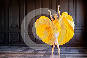 Elegant ballerina in pointe shoes dances with flowing yellow fabric on a dark gray background
