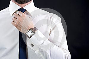 Elegant bearded man in white shirt tying up necktie.