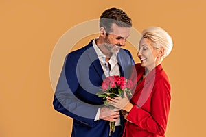 Elegant beautiful couple in love on a date. Smiling handsome man and attractive blonde woman posing together with red roses