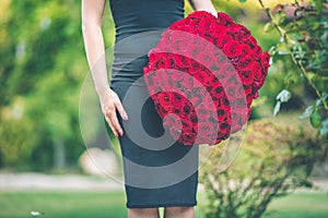 Elegant beautiful woman is wearing black fashion dress is holding big bouquet of 101 red roses