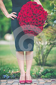 Elegant beautiful woman is wearing black fashion dress is holding big bouquet of 101 red roses