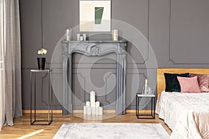 Elegant bedroom interior with a candles set in a fireplace portal, metal tables, wall molding and bed