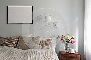 Elegant bedroom. Tulips, cherry tree blossoms bouquet in glass vase. Wooden night stand. Cup of coffee. Blank black
