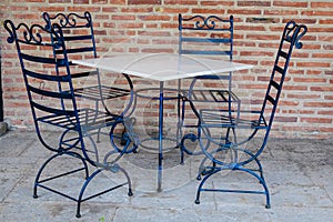 Elegant black metallic chairs and one white table near a red bricks wall in a garden in a sunny spring day, in Bucharest, Romania