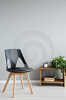 Elegant black wooden chair next to cabinet with clock and flowers in modern office interior