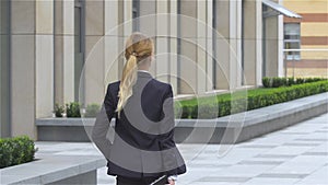 Elegant blonde business woman with tablet computer goes around office building. slow motion