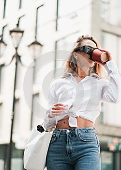 Elegant Blonde Woman Drinking Coffee While Walking Outdoors, Confident Female Entrepreneur Wearing Sunglasses and Golden