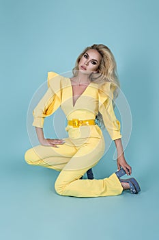 Elegant blonde woman in stylish yellow jumpsuit and fashionable accessories on color background. Beautiful fashion model on blue