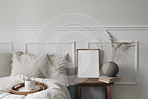 Elegant boho bedroom interior. Vertical wooden picture frame mockup on old bedside table. Cup of coffee. Ball vase with