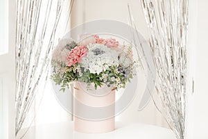 An elegant bouquet of fresh roses, peonies, and daisies in a pink box, beautifully arranged and placed by a light-filled