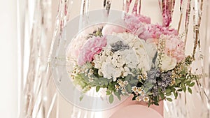 An elegant bouquet of fresh roses, peonies, and daisies in a pink box, beautifully arranged and placed by a light-filled