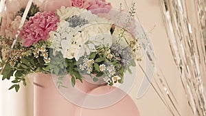 An elegant bouquet of fresh roses, peonies, and daisies in a pink box, beautifully arranged and placed by a light-filled