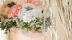 An elegant bouquet of fresh roses, peonies, and daisies in a pink box, beautifully arranged and placed by a light-filled