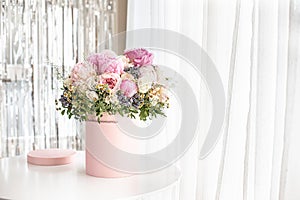 An elegant bouquet of fresh roses, peonies, and daisies in a pink box, beautifully arranged and placed by a light-filled