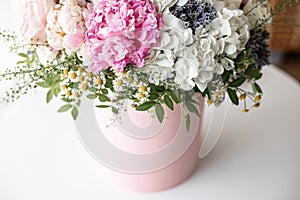 An elegant bouquet of fresh roses, peonies, and daisies in a pink box, beautifully arranged and placed by a light-filled