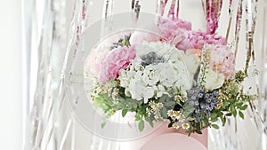 An elegant bouquet of fresh roses, peonies, and daisies in a pink box, beautifully arranged and placed by a light-filled