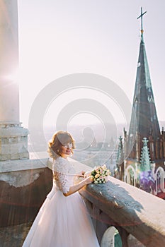 Elegant bride poses on the tower balcony of antique gothic cathedral