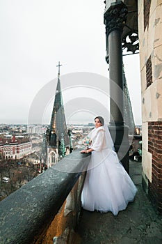 Elegant bride poses on the tower balcony of old gothic cathedral