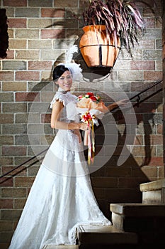 Elegant bride with wedding bouquet over brick wall