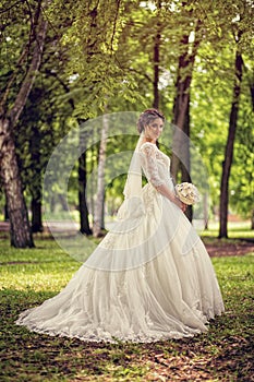 Elegant bride in wedding dress with dipped hem in full length on a background of a forest or Park