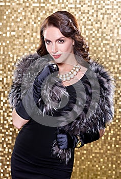 Elegant brunette retro woman wearing silver fox fur over gold mosaic background. Model looking at the camera