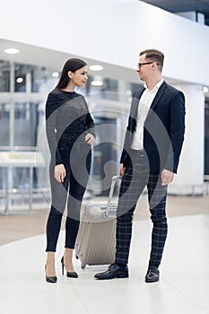 Elegant business couple standing with suitcase and airplane tickets at the waiting hall in the airport. Business travel