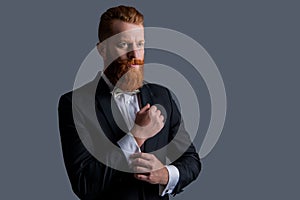 Elegant businessman adjusting cuffs. Bearded businessman wearing tuxedo. Businessman with beard