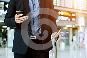 Elegant businessman checking e-mail on mobile phone while walking with suitcase inside airport