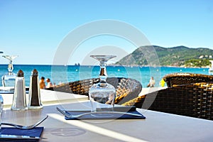 Elegant cafe with sea view on French Riviera is waiting for guests, served lunch table with glasses, tableware and napkins