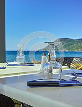 Elegant cafe with sea view on French Riviera is waiting for guests, served lunch table with glasses, tableware and napkins