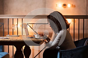 Elegant caucasian businesswoman sitting at modern restaurant working on her laptop and drinking coffee.