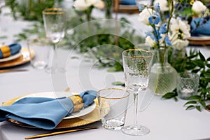 Elegant and chic wedding table setting in gold and blue colors and fresh flowers. Soft selective focus